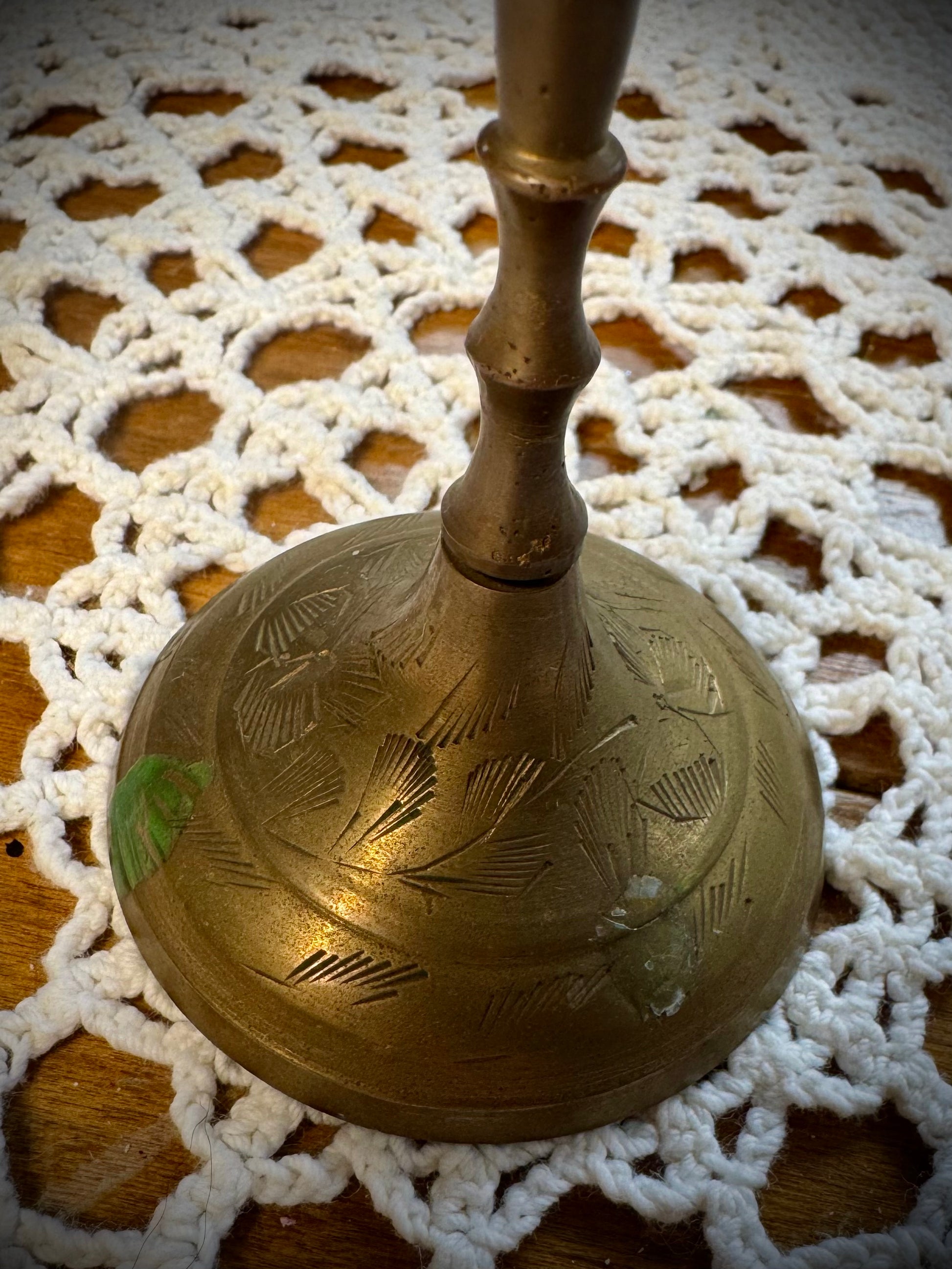 A vintage brass candle holder with etching on the base, displayed on a white lace tablecloth.