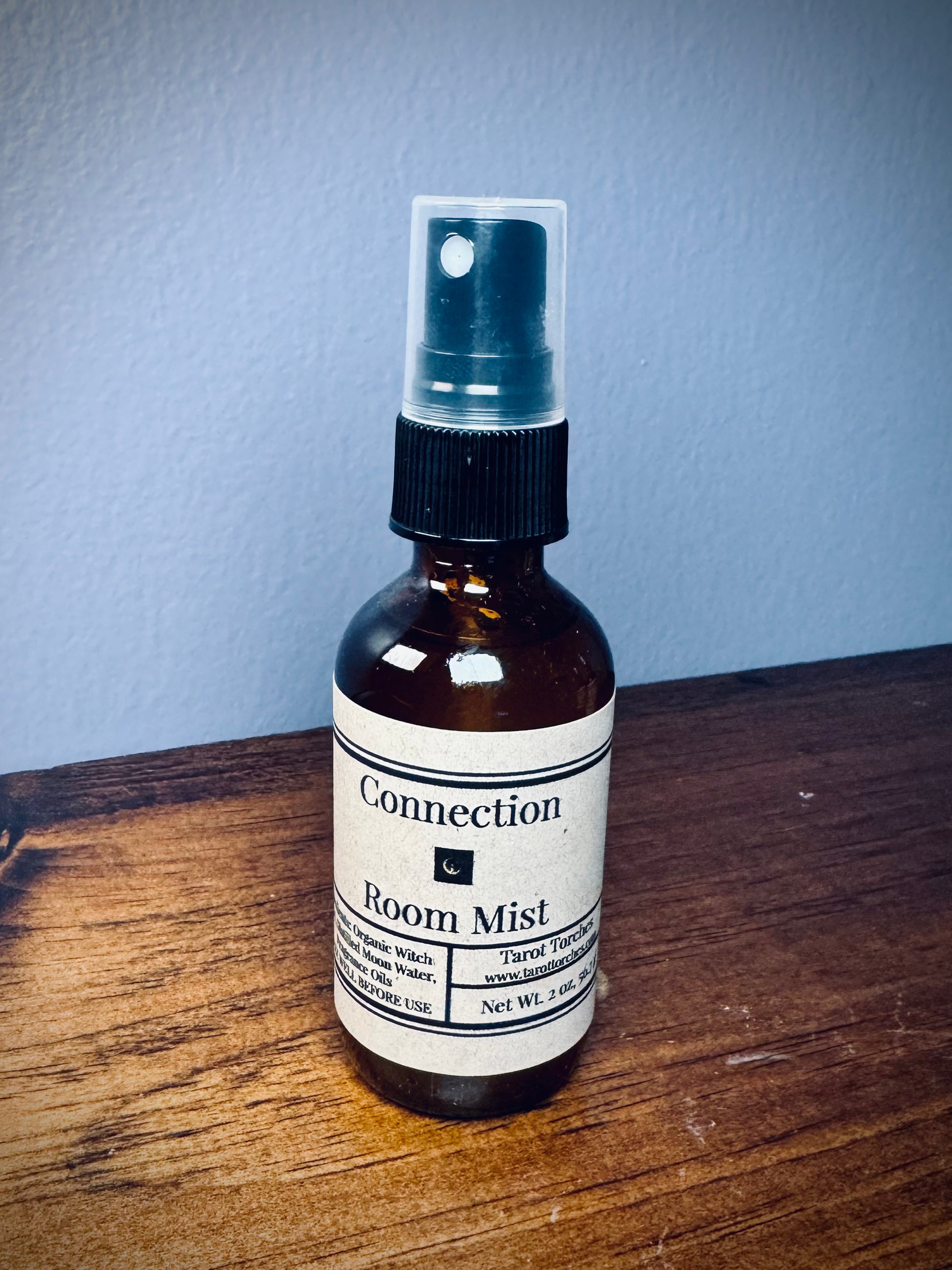 An amber glass spray bottle with a label reading "Connection" on a wooden surface.