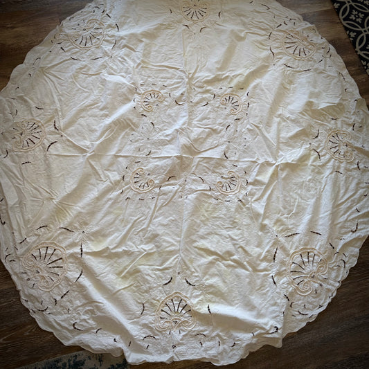 A vintage round tablecloth with a floral pattern, predominantly ivory in color with yellowing and visible staining.