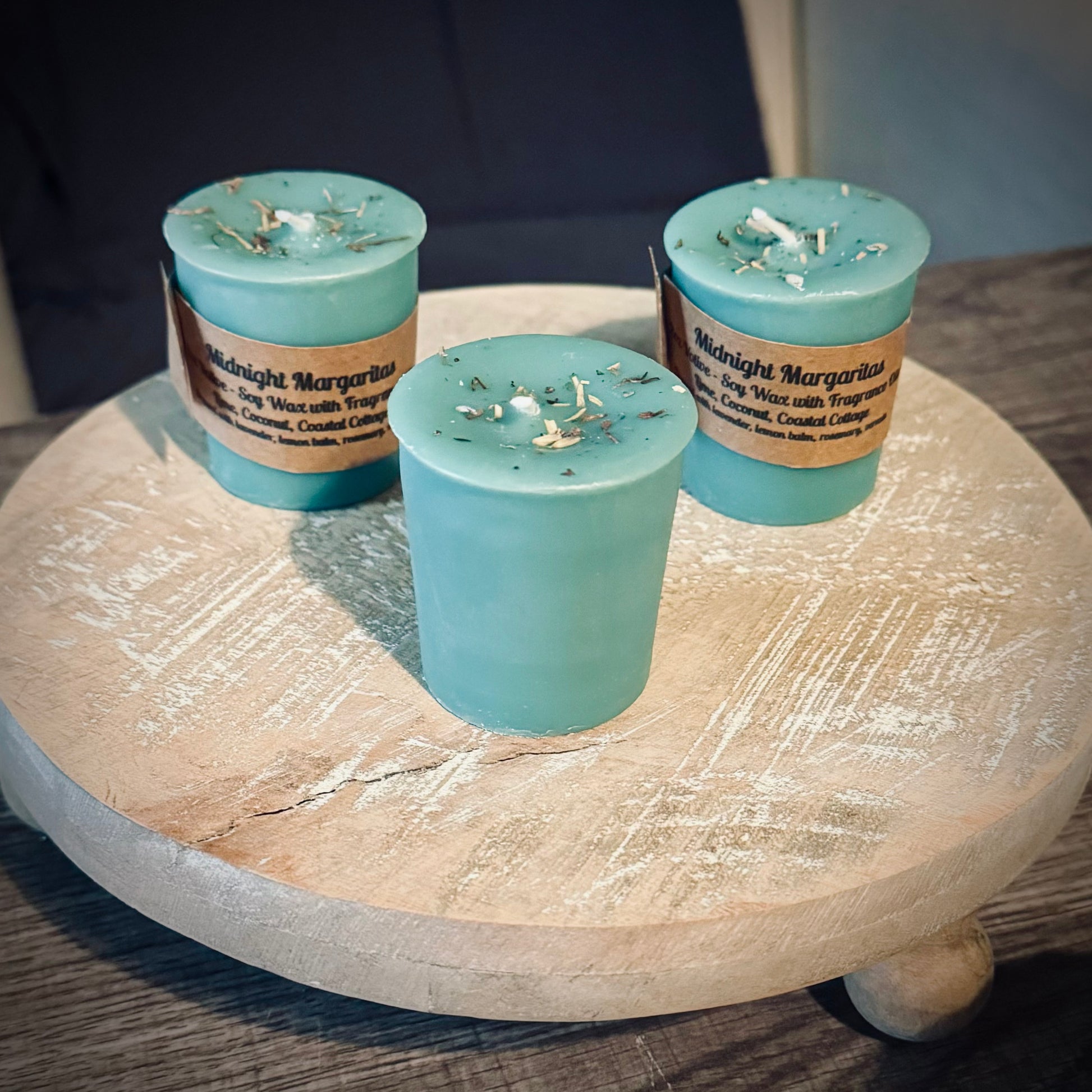 A set of three green votive candles, two with brown kraft labels sitting on a wooden surface.