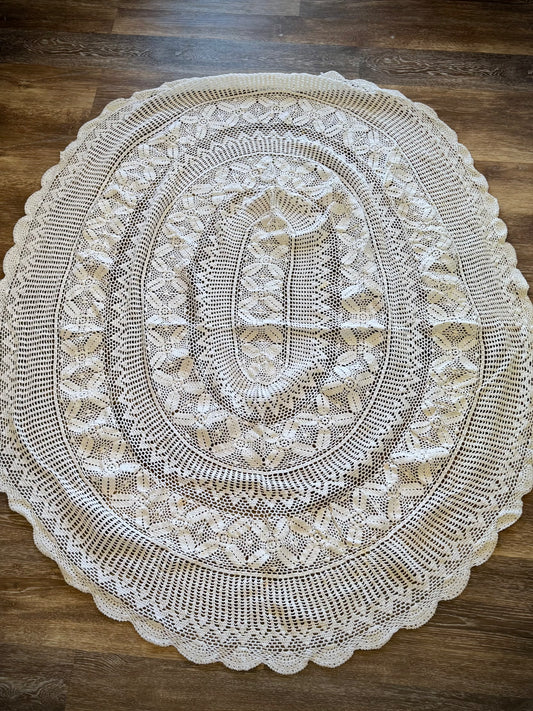 A vintage white crochet tablecloth with an oval shape, displayed on a wooden surface.