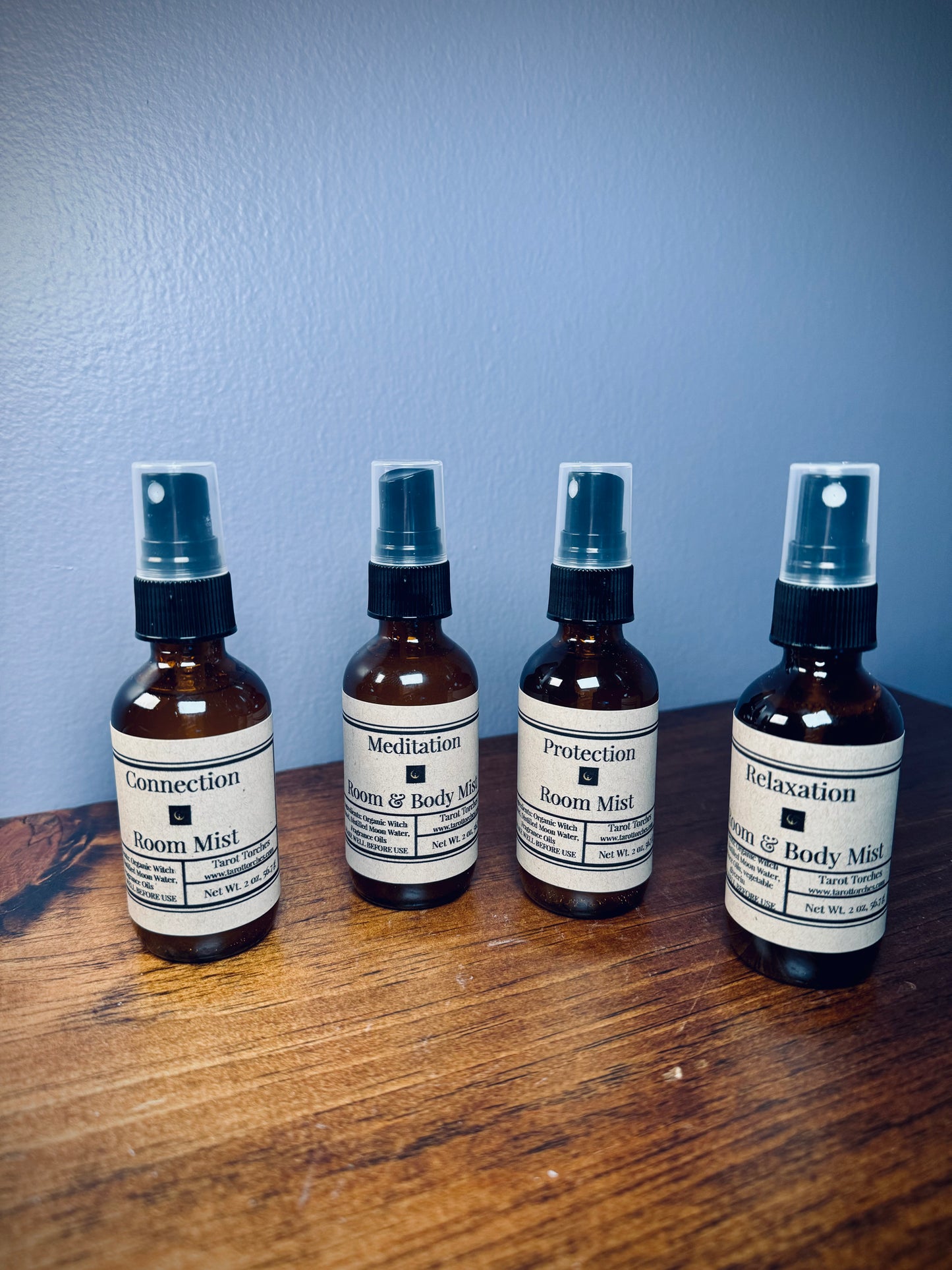 A set of four amber glass spray bottles with kraft labels on a wooden surface.