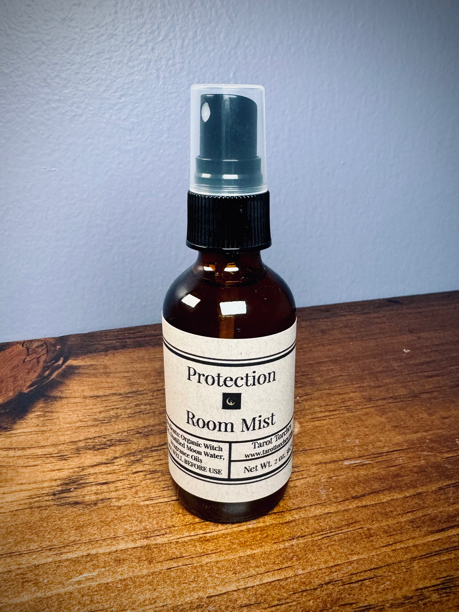 An amber glass spray bottle with a label reading "Protection" on a wooden surface.