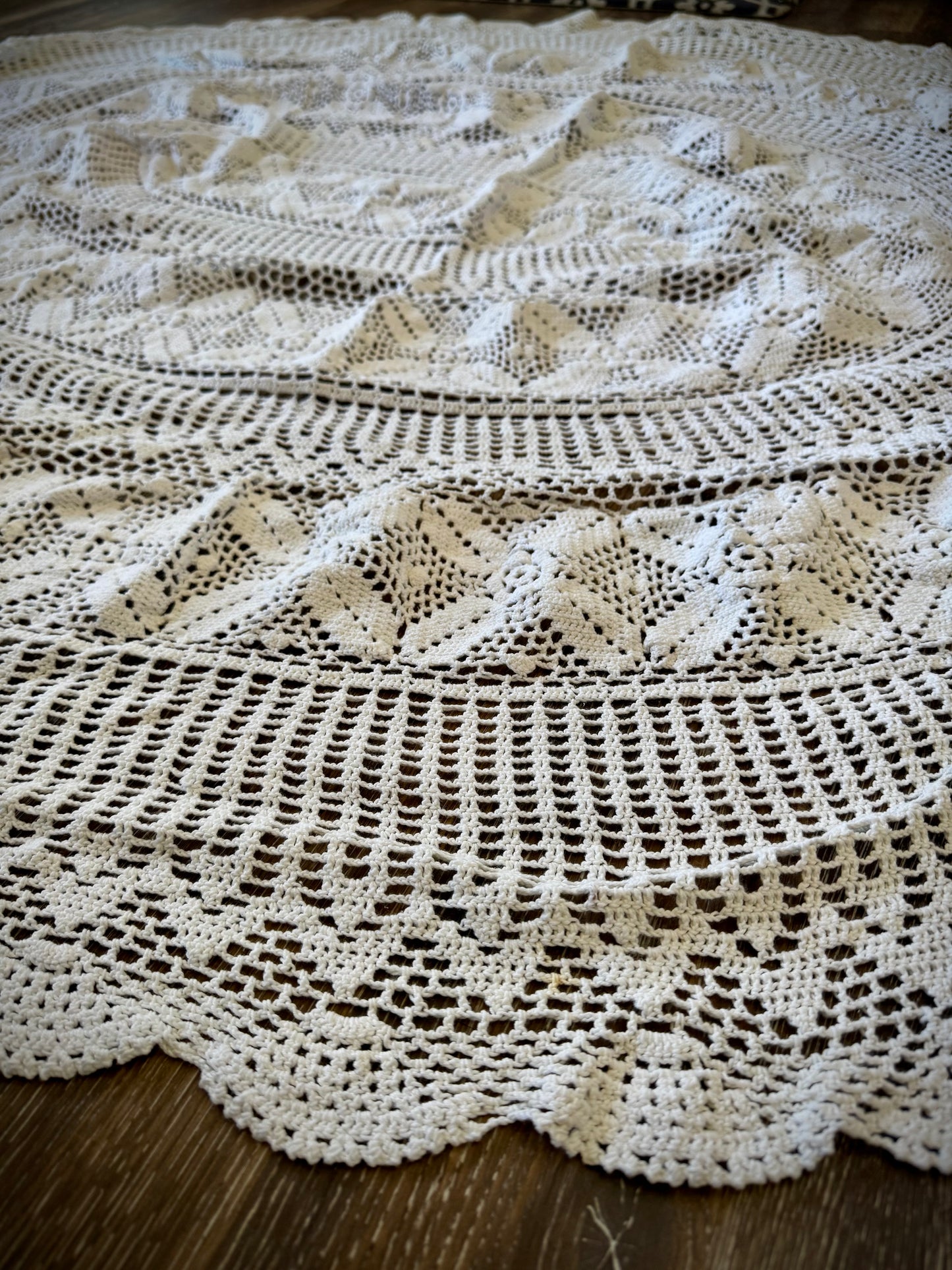 A vintage white crochet tablecloth with an oval shape, displayed on a wooden surface.