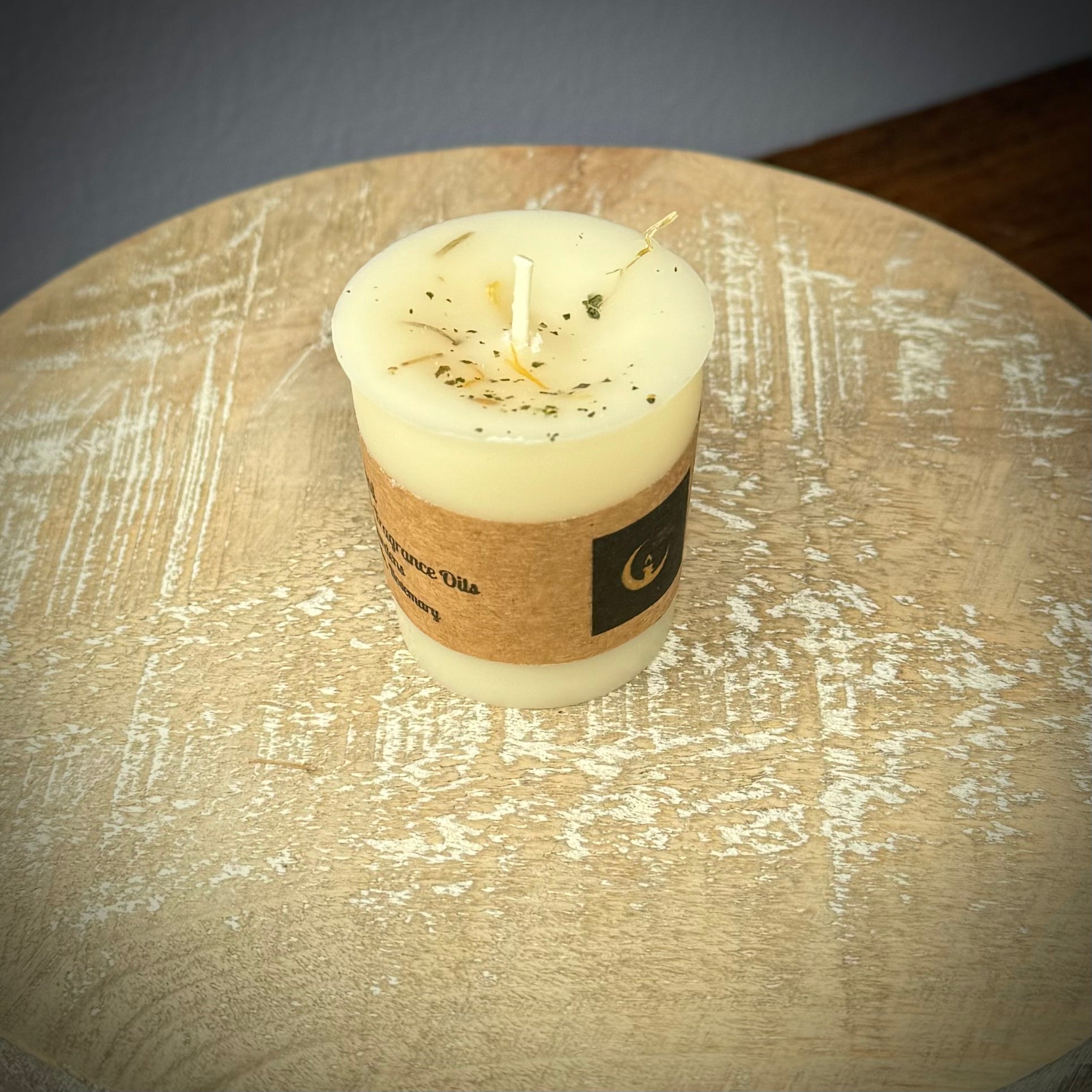 A white votive candle with a kraft label on a white wooden surface.