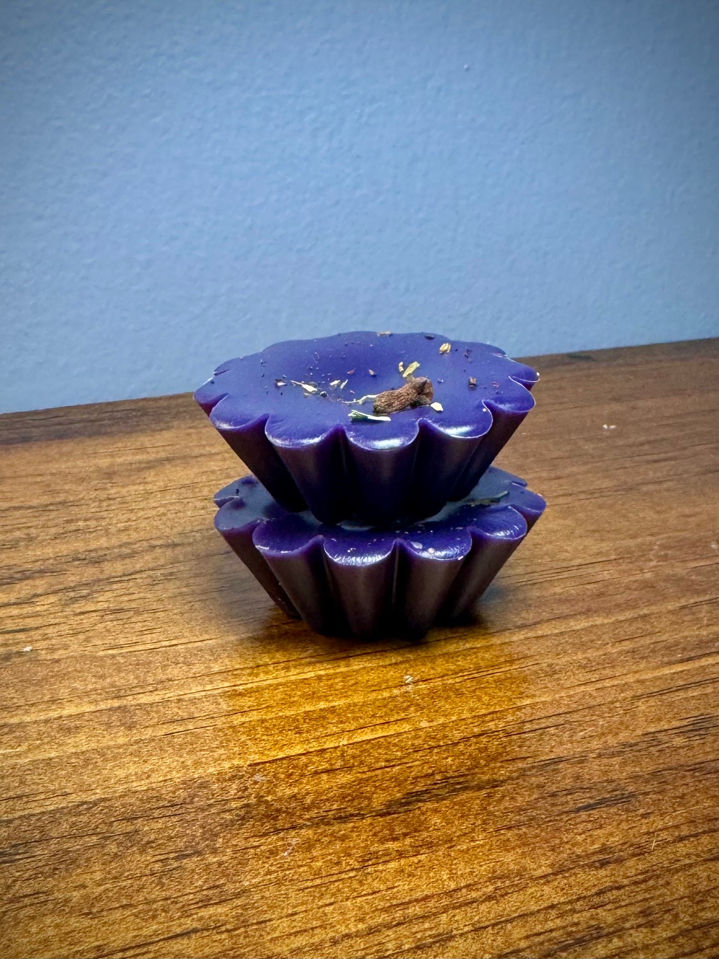 A stack of two purple soy wax tarts with visible herbs on a wooden surface.
