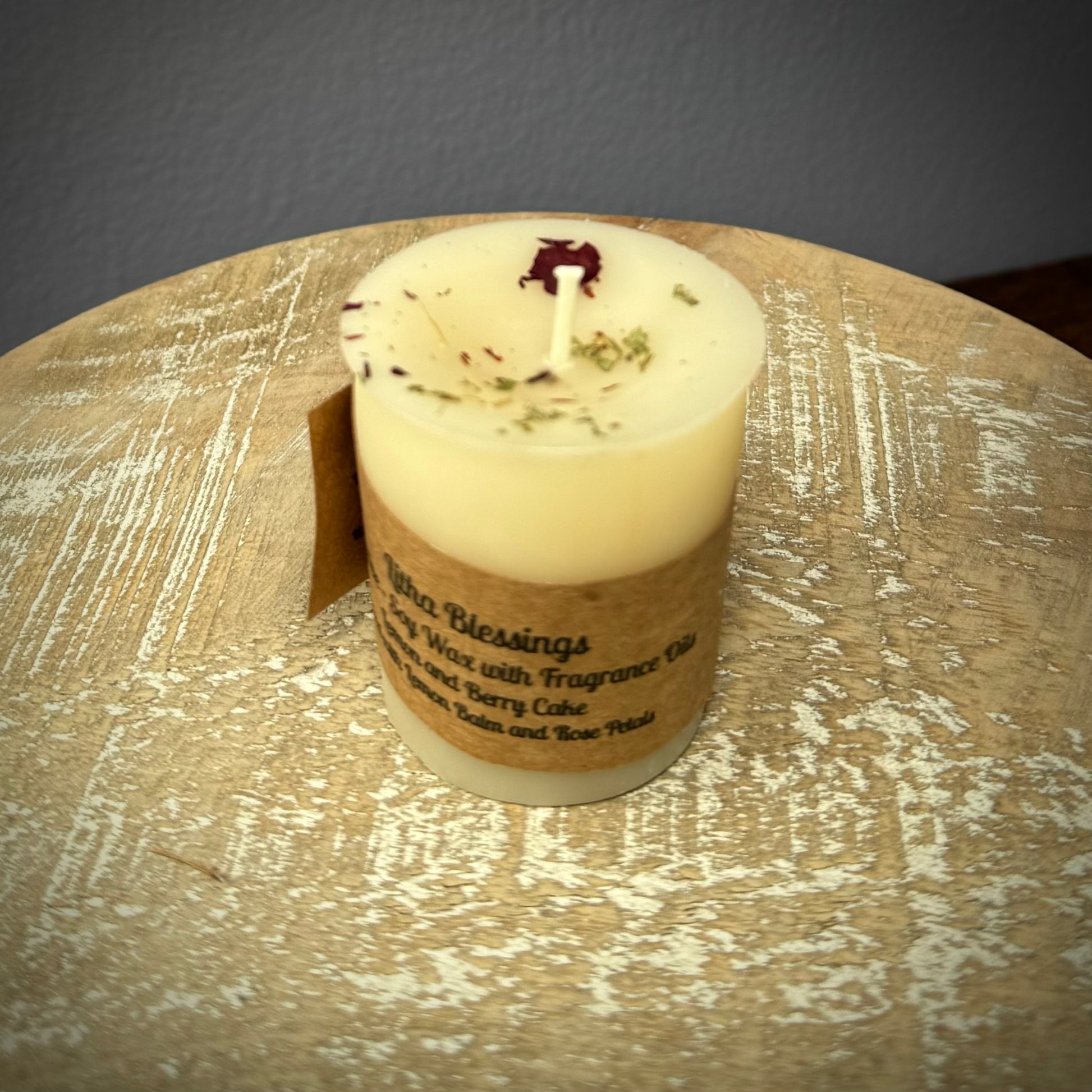 A white votive candle with a kraft label on a white wooden surface.