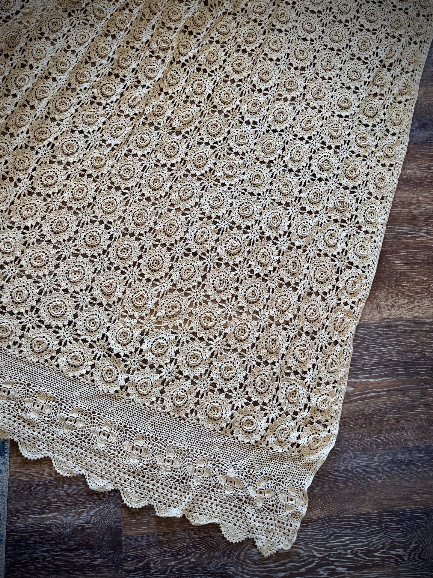 A beige crochet coverlet featuring a floral rosette pattern and a scalloped edge.