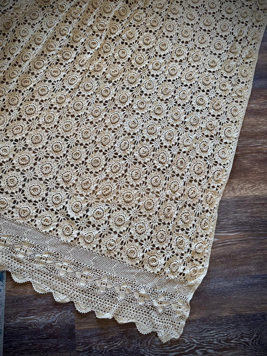 A beige crochet coverlet featuring a floral rosette pattern and a scalloped edge.