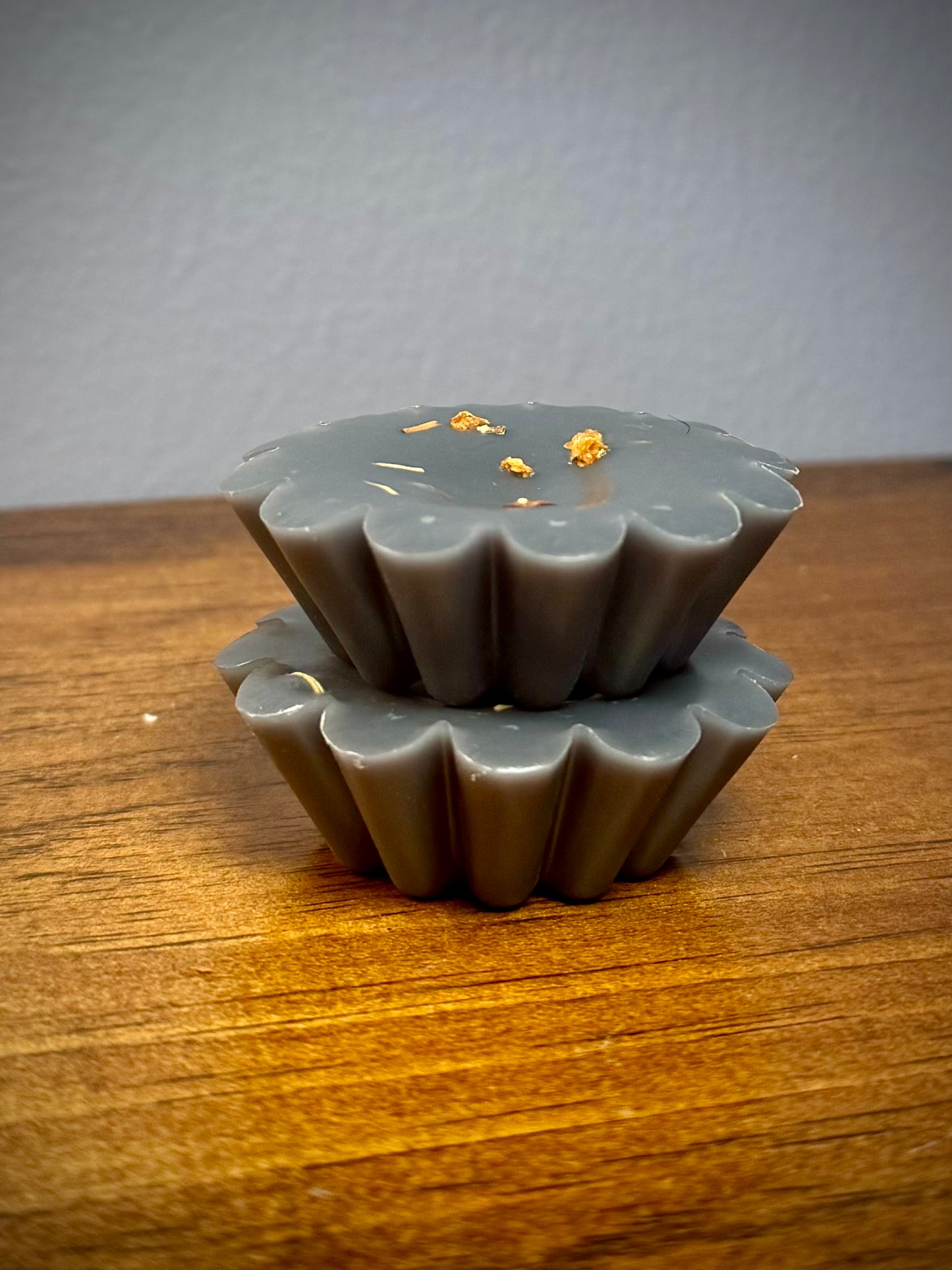 A stack of two black soy wax tarts with visible herbs on a wooden surface.