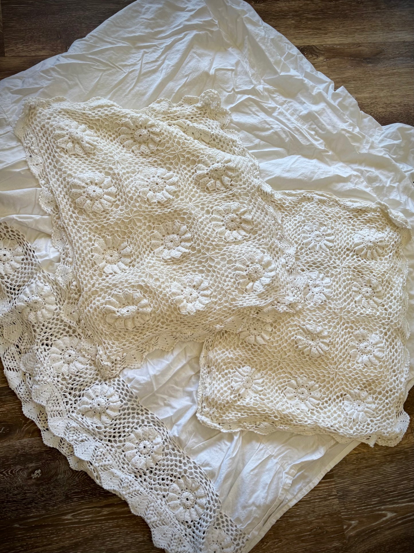 A vintage crochet bed skirt and two pillowcases laid out on a flat surface.