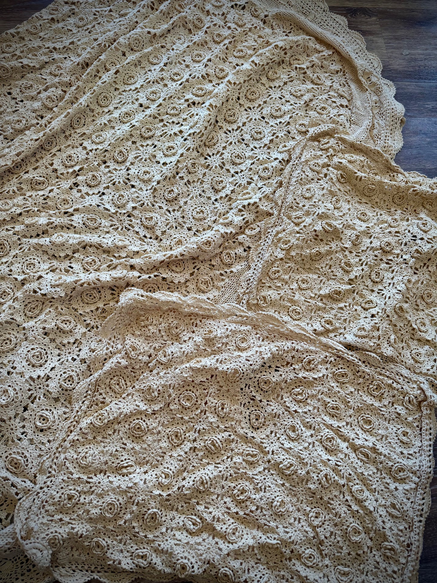 A beige crochet coverlet and two pillowcases featuring a floral rosette pattern and a scalloped edge.