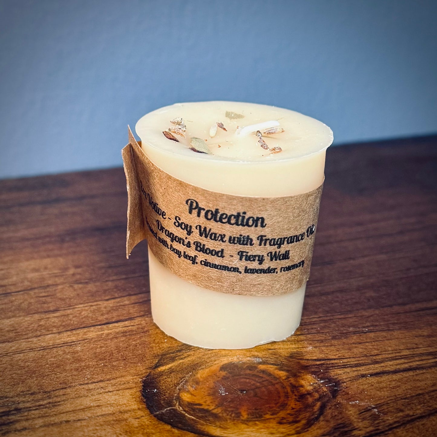 A white votive candle with natural soy wax  labeled 'Protection' placed on a wooden surface.