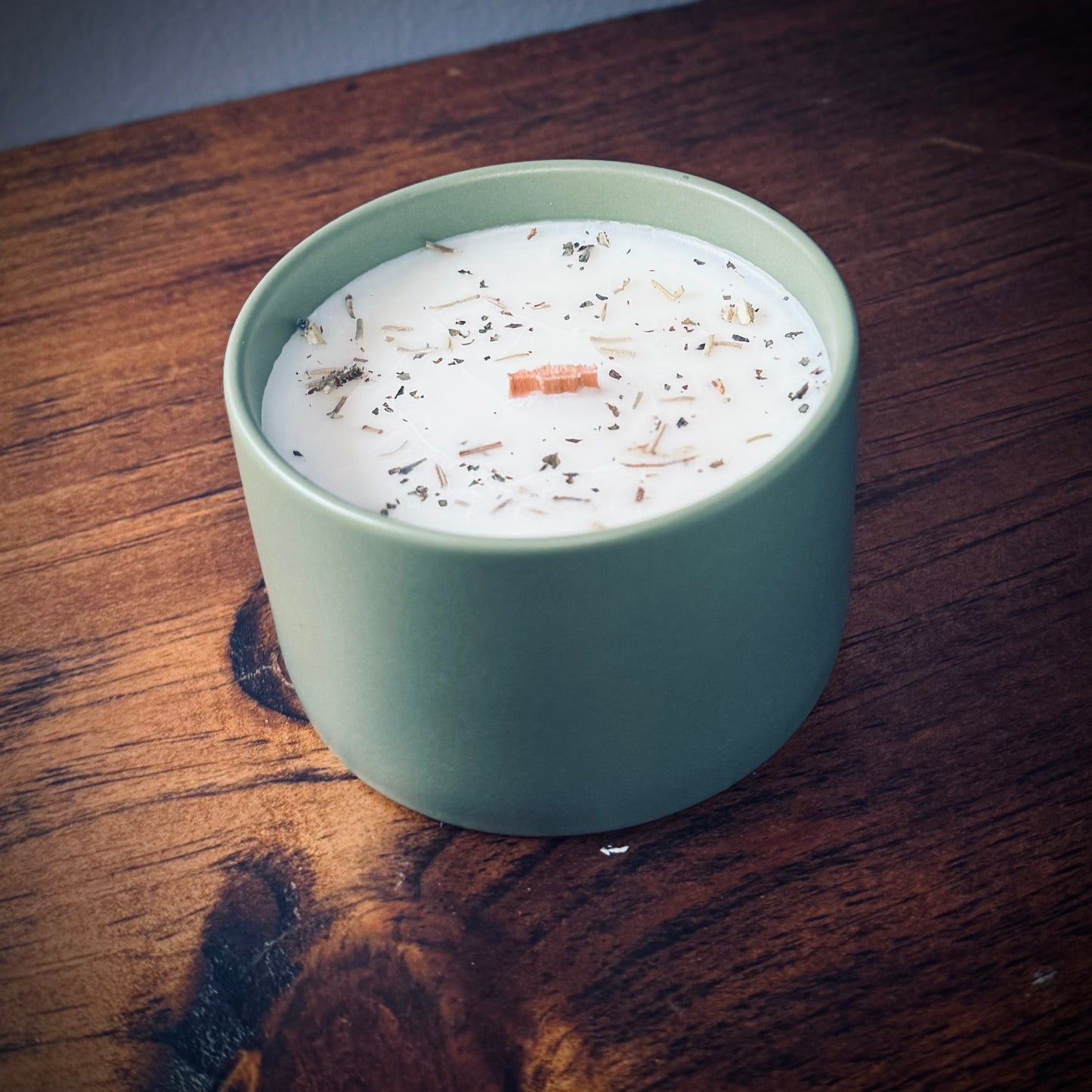 Green ceramic candle with lid off showcasing a wooden wick on a wooden surface