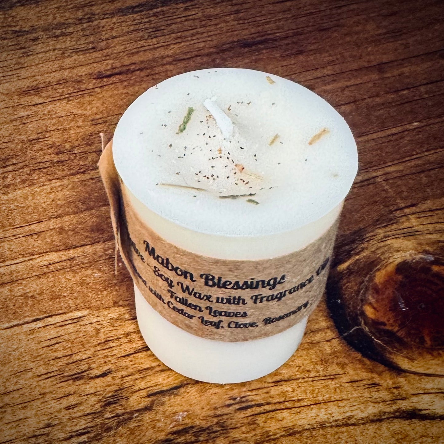 A white votive candle with a label reading "Mabon Blessings" on a wooden surface.