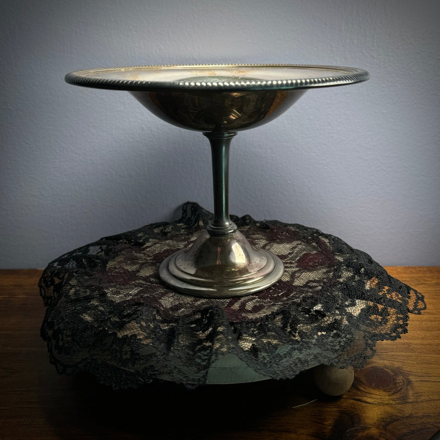 A vintage silver plate bowl with a step and round base sits on a black doily