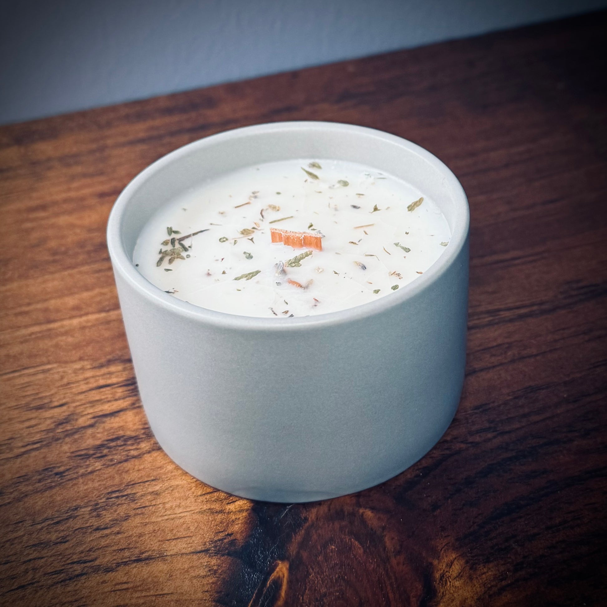 Gray ceramic candle with lid off showcasing a wooden wick on a wooden surface