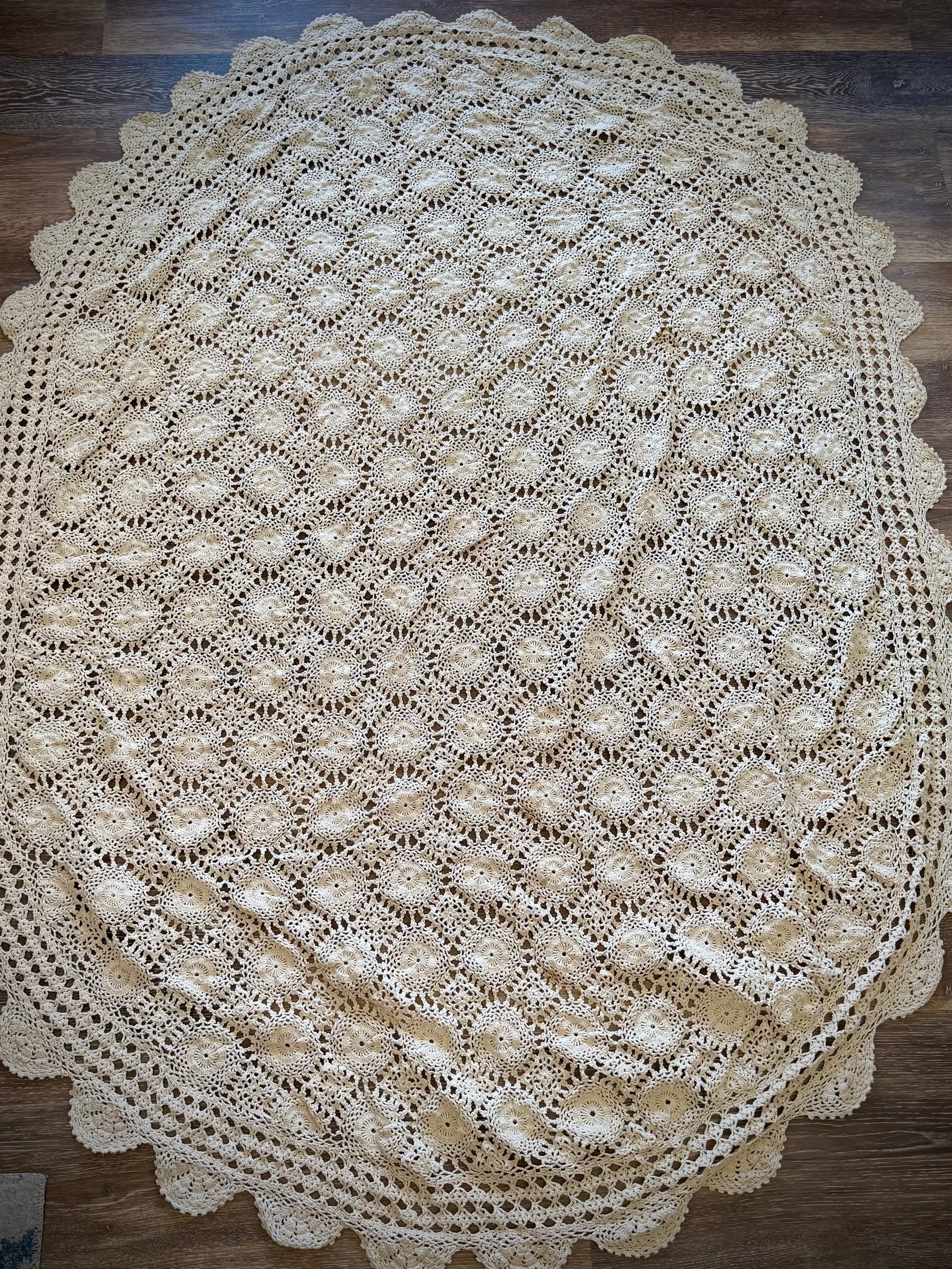 A vintage oval crochet tablecloth with an oval shape and a ivory color, displayed on a wood surface.