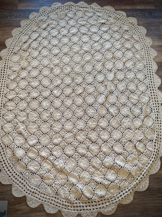 A vintage oval crochet tablecloth with an oval shape and a ivory color, displayed on a wood surface.