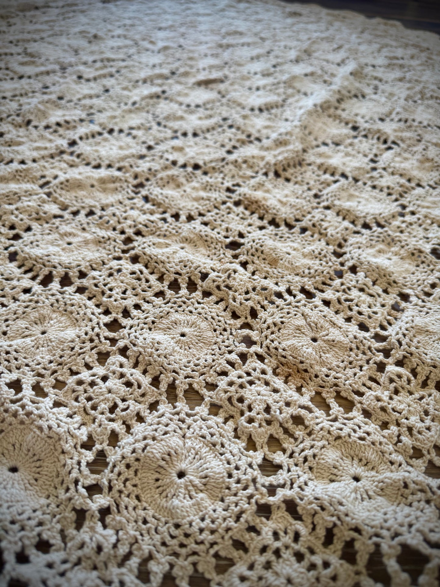 A close up of detailed crochet embroidery on an ivory tablecloth