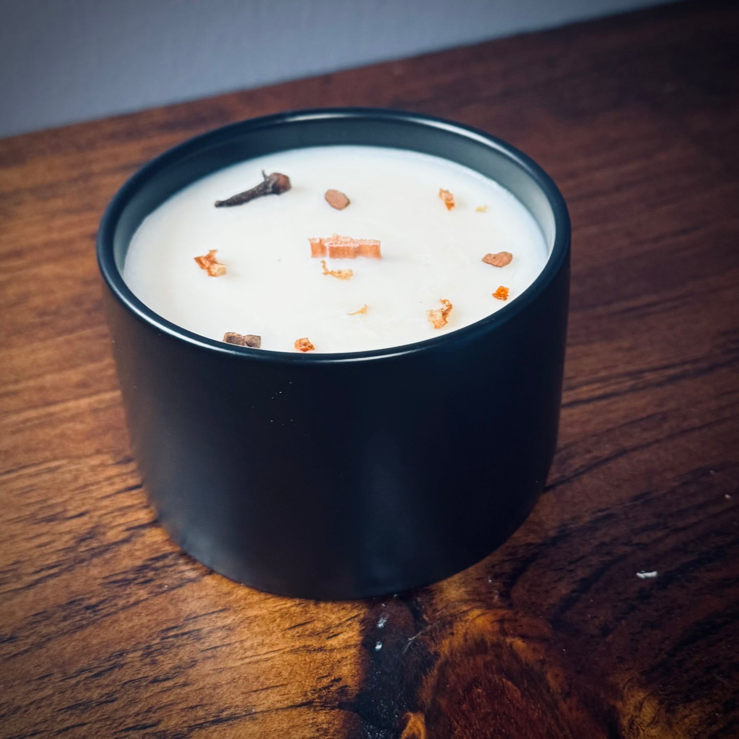 Black ceramic candle with lid off showcasing a wooden wick on a wooden surface