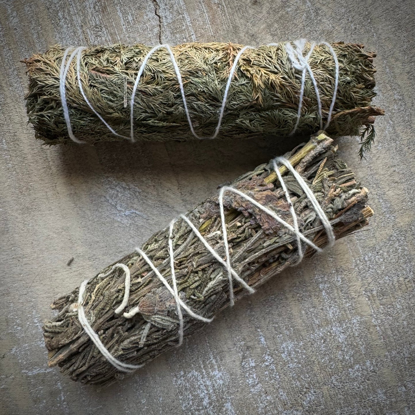 Two herbal bundles tied with string, one green and one brown, placed on a light surface.