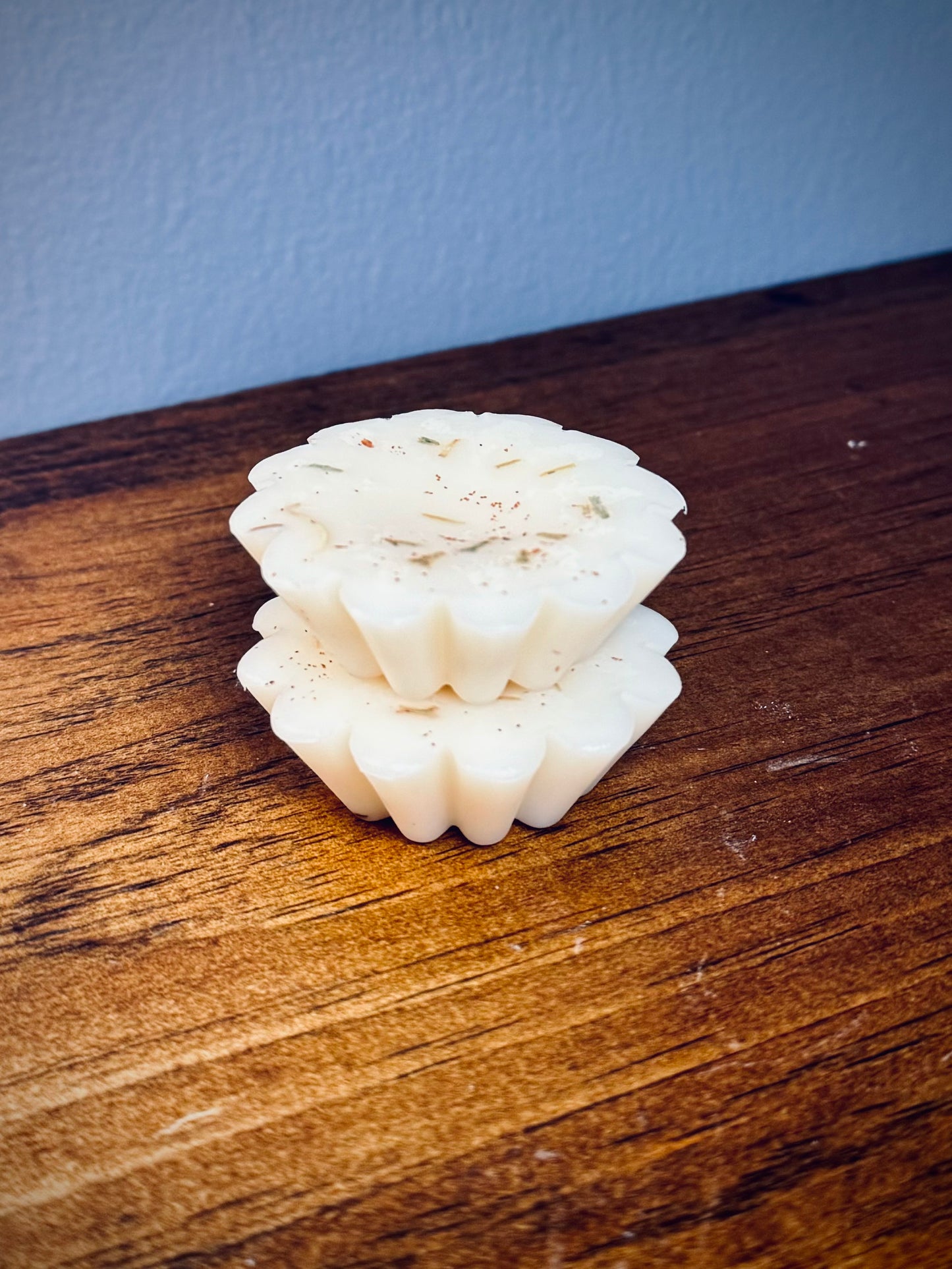 A stack of two white soy wax tarts with visible herbs on a wooden surface.