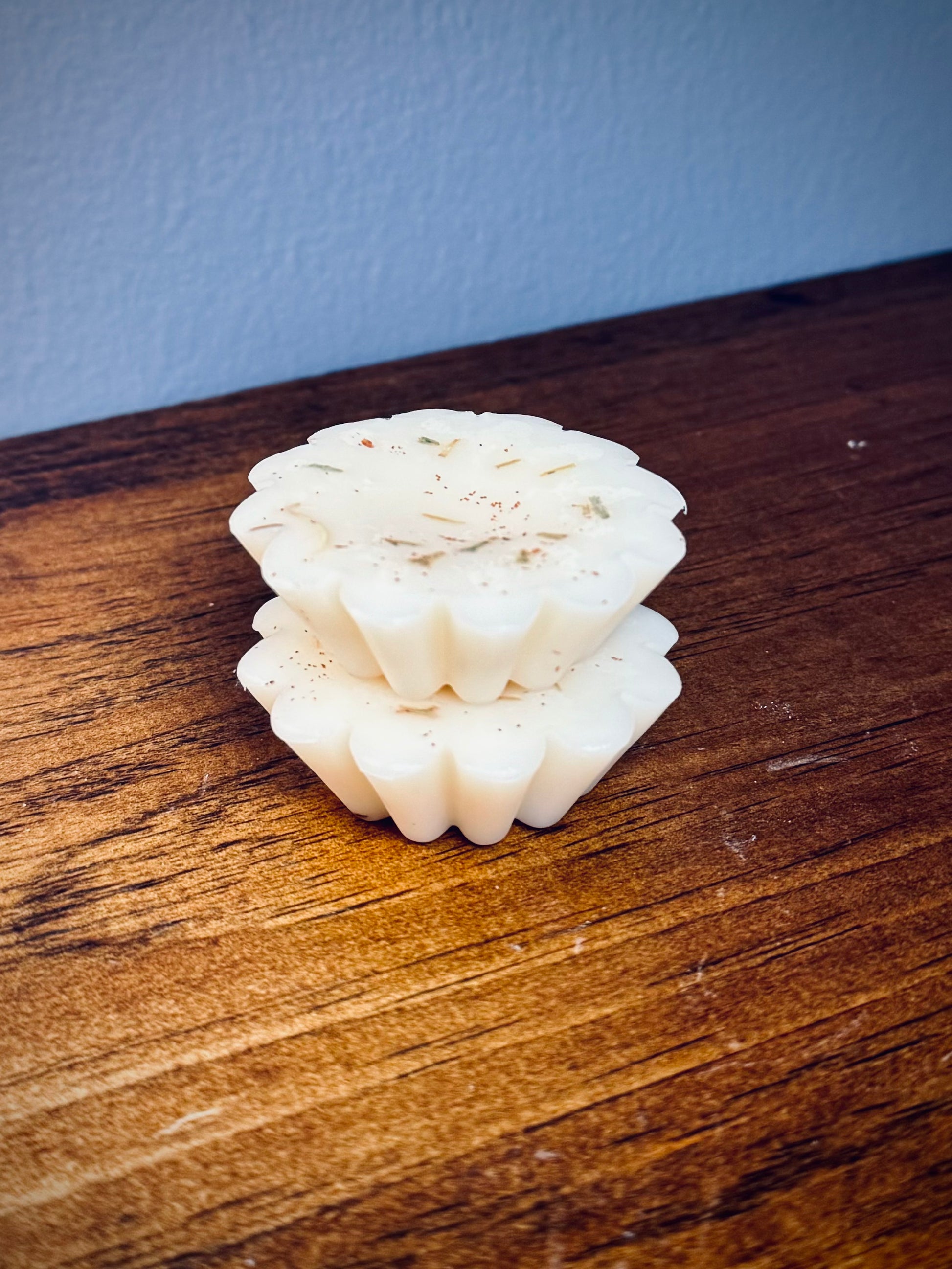 A stack of two white soy wax tarts with visible herbs on a wooden surface.