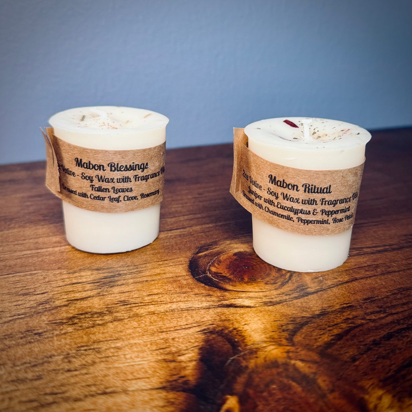 A set of two white votive candles with brown craft labels reading "Mabon Blessings" and "Mabon Ritual" on a wooden surface.