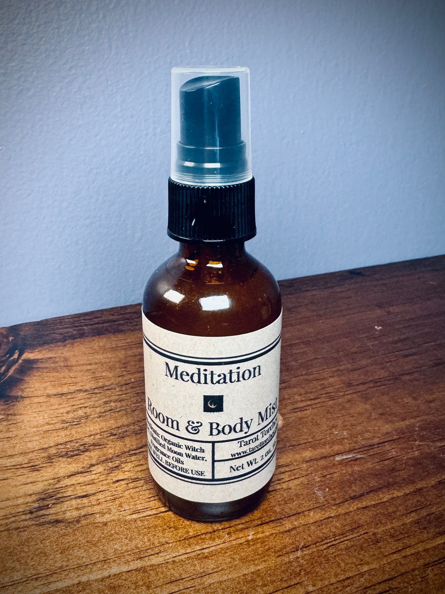 An amber glass spray bottle with a label reading "Meditation" on a wooden surface.