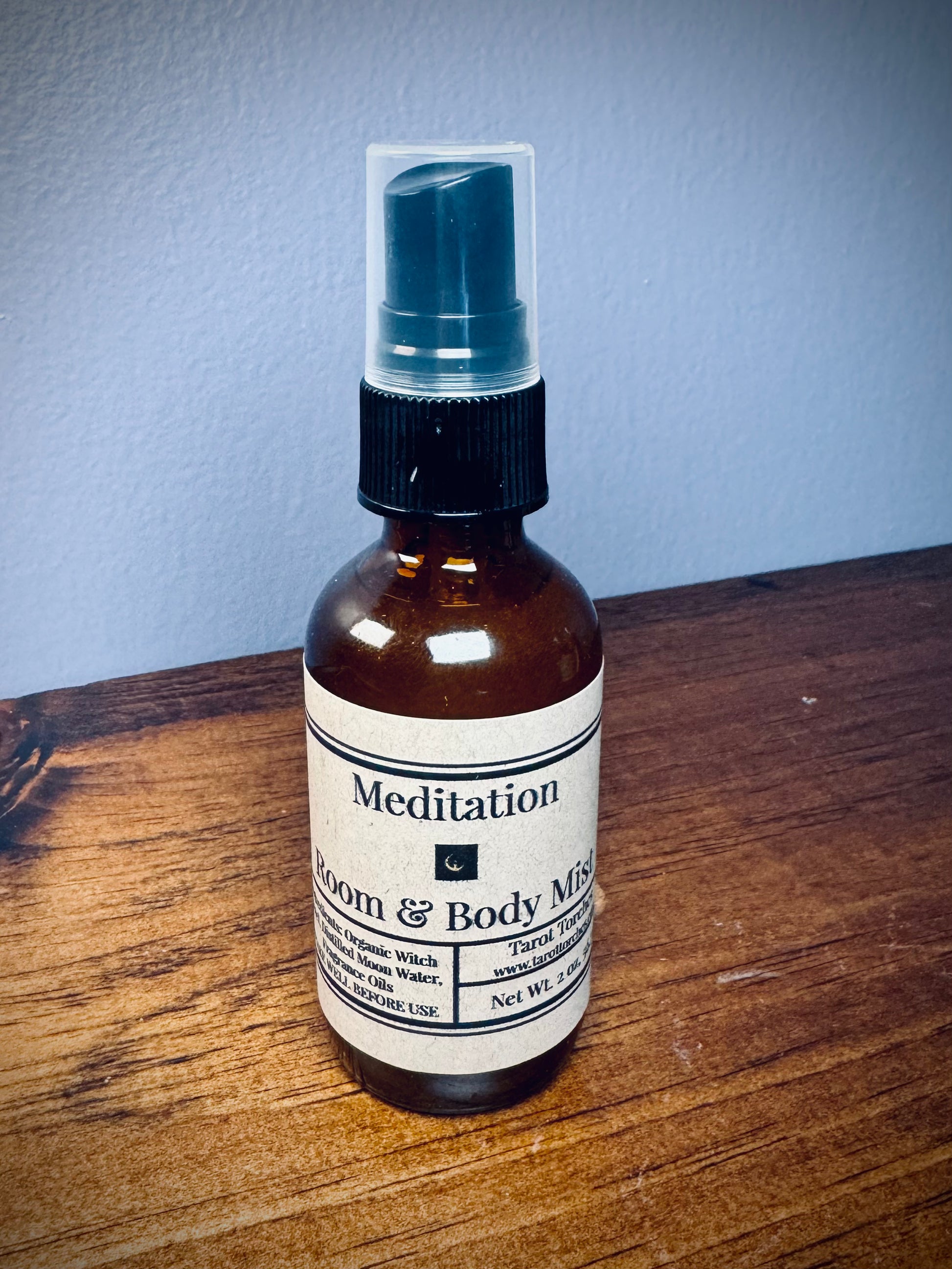 An amber glass spray bottle with a label reading "Meditation" on a wooden surface.