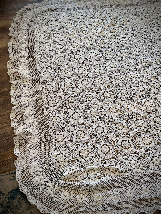 A vintage white crochet blanket with a geometric pattern displayed on a wooden floor.