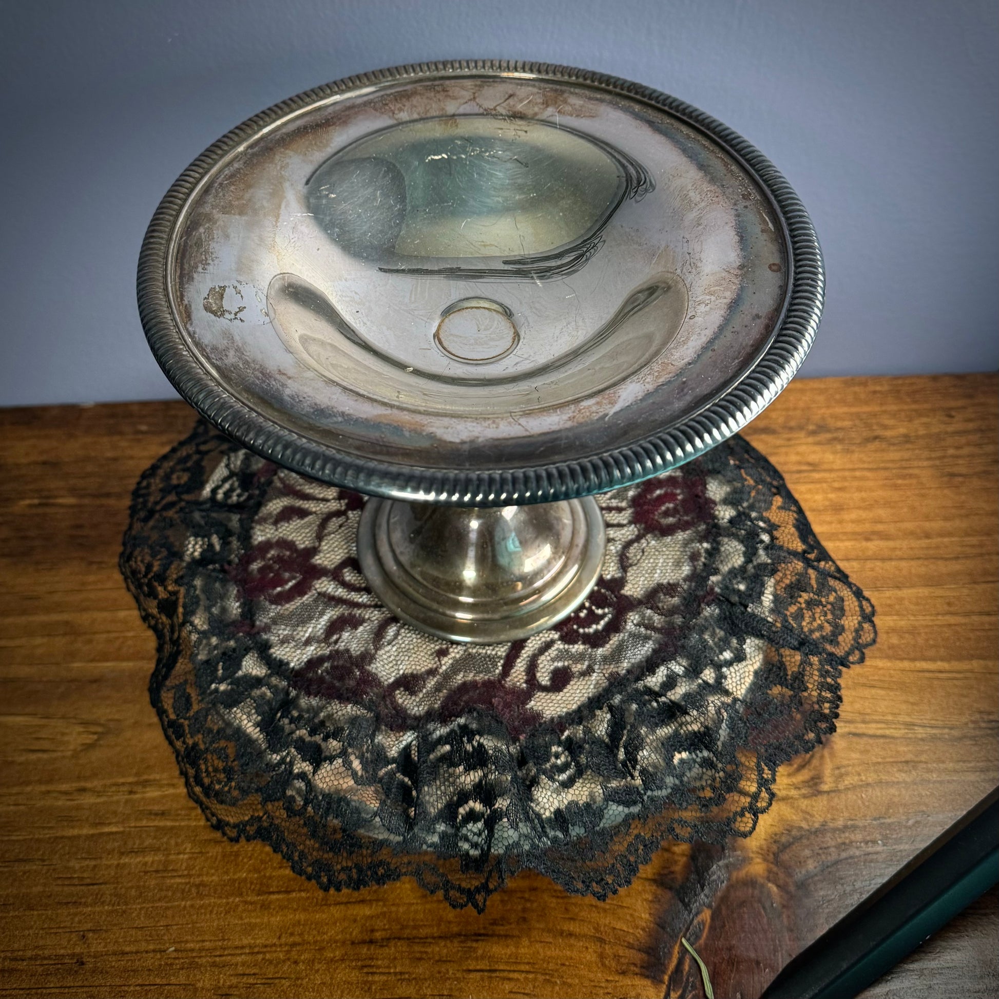 A vintage silver plate bowl with a step and round base sits on a black doily