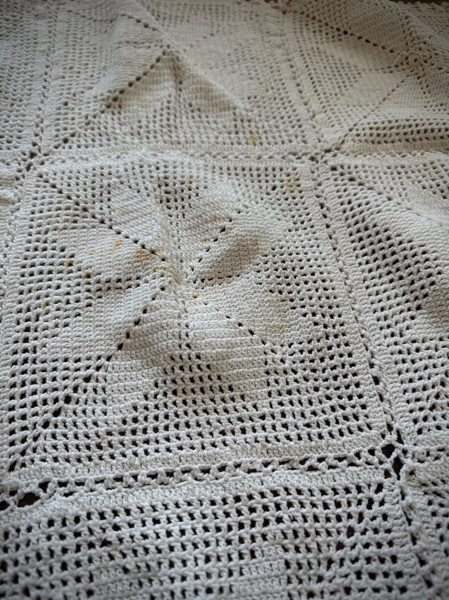 Close up of a vintage crochet altar cloth laid out flat, primarily in off-white color with a geometric pattern.