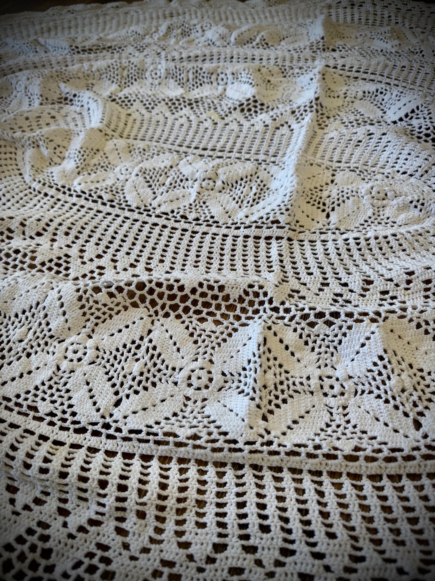 A vintage white crochet tablecloth with an oval shape, displayed on a wooden surface.