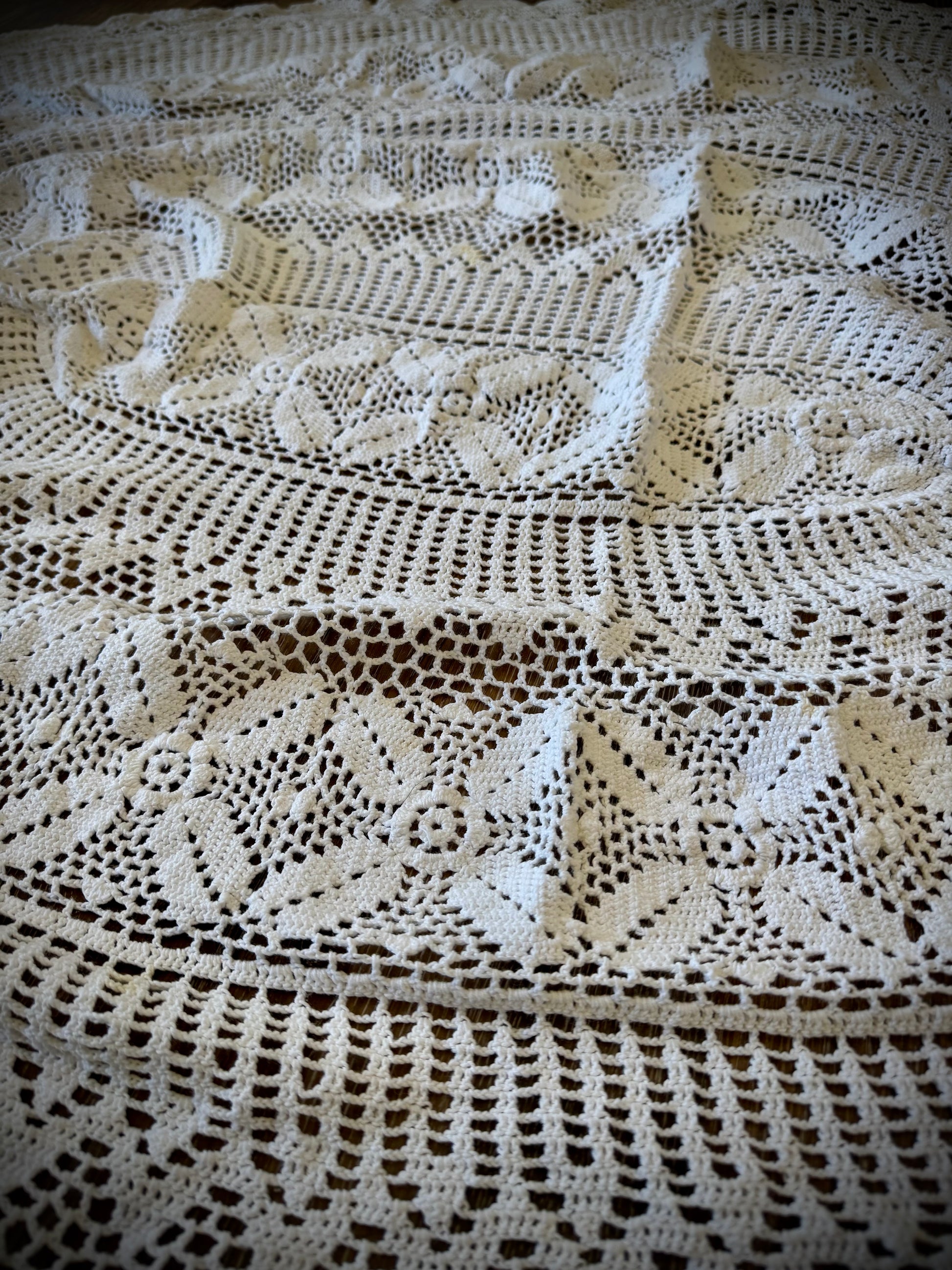 A vintage white crochet tablecloth with an oval shape, displayed on a wooden surface.
