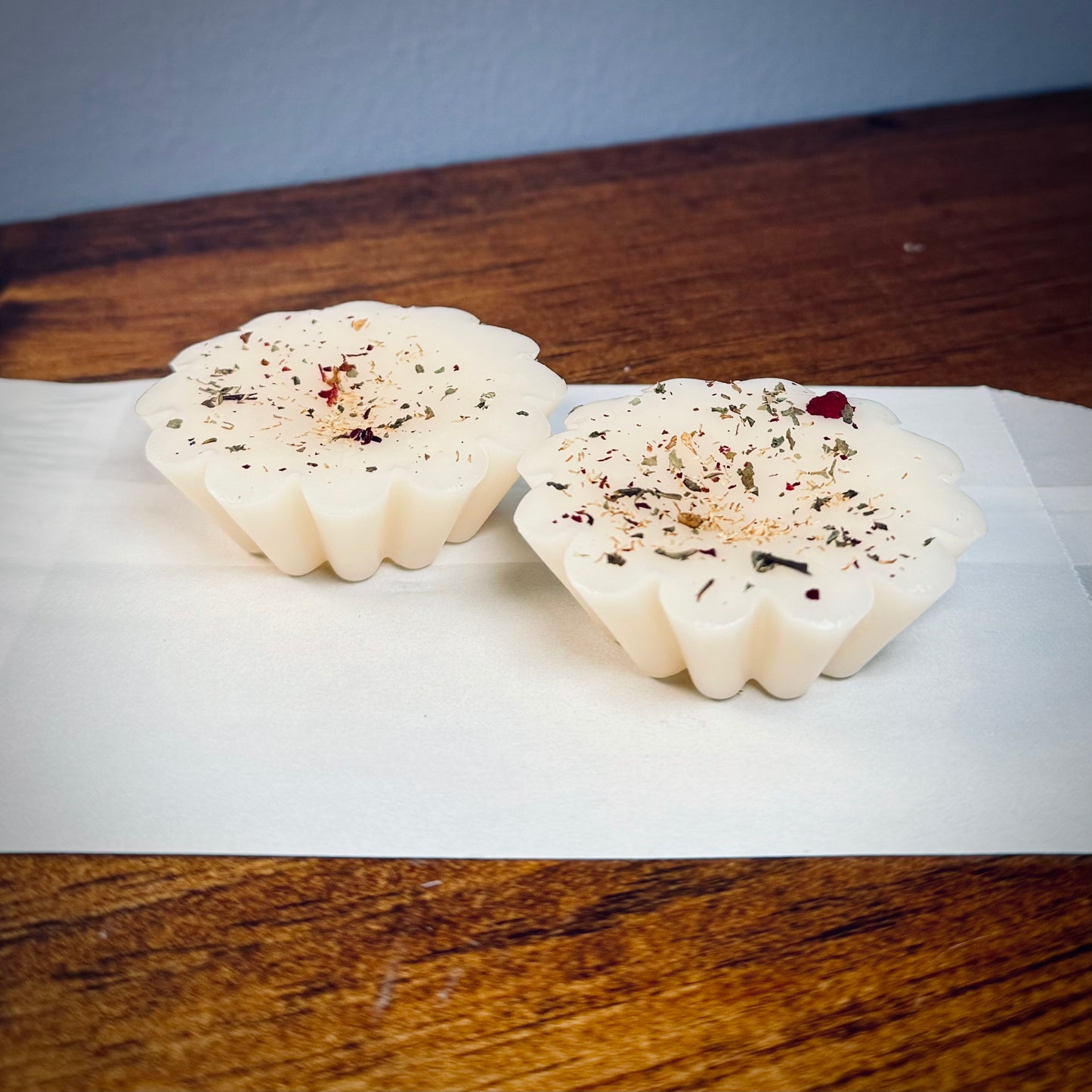 A set of two white soy wax tarts with visible herbs on top of a white bag.