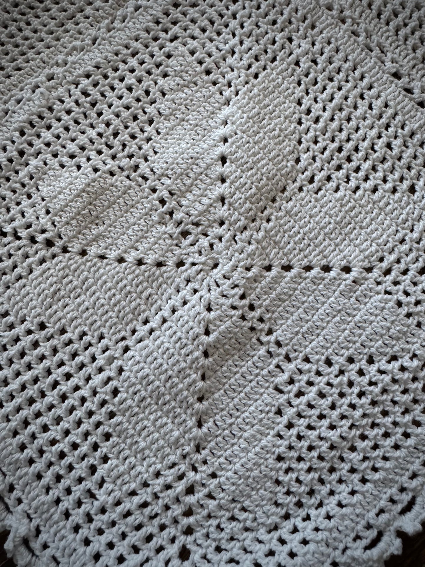 Extreme close up of a vintage crochet altar cloth laid out flat, primarily in off-white color with a geometric pattern.