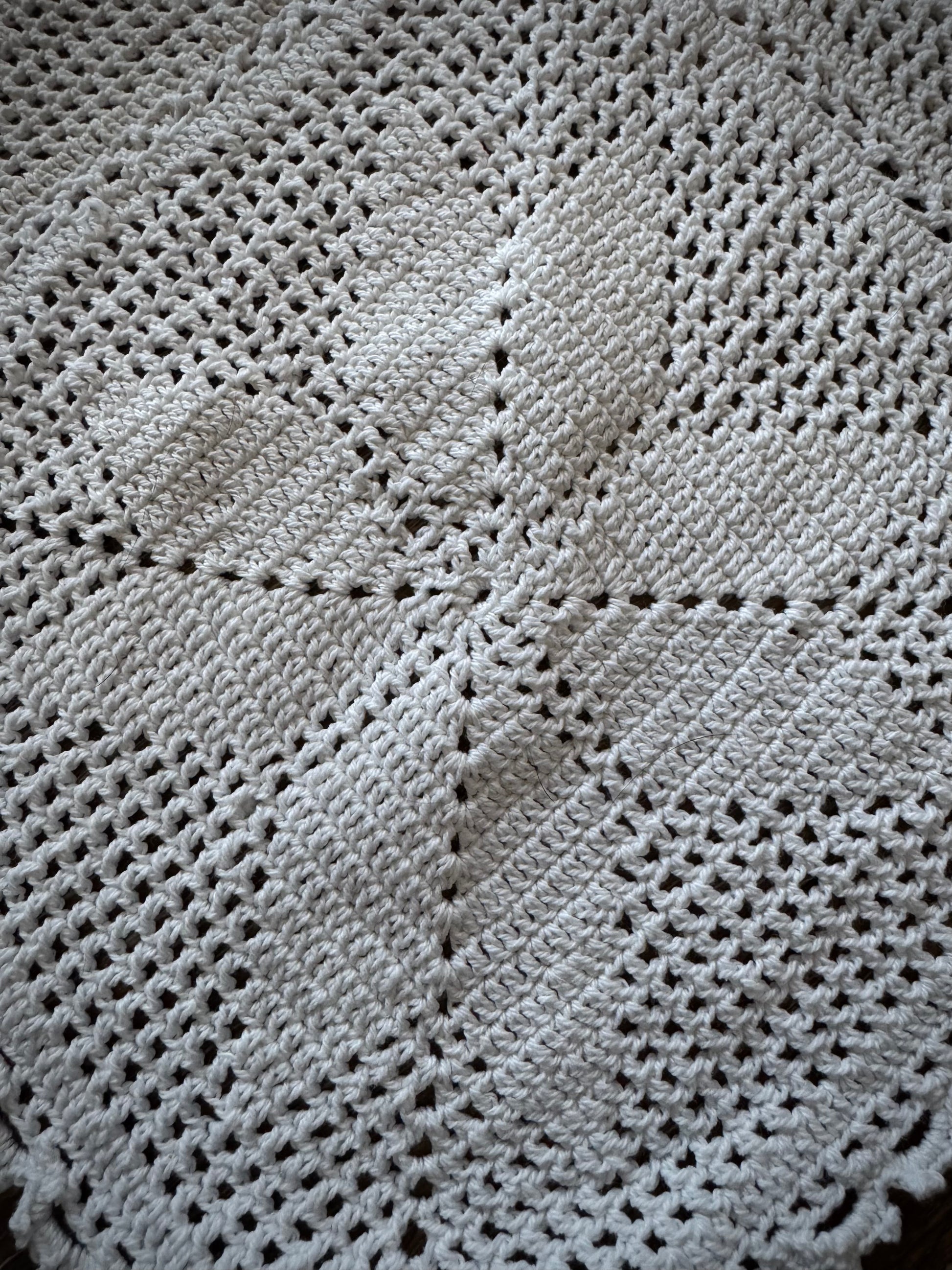 Extreme close up of a vintage crochet altar cloth laid out flat, primarily in off-white color with a geometric pattern.