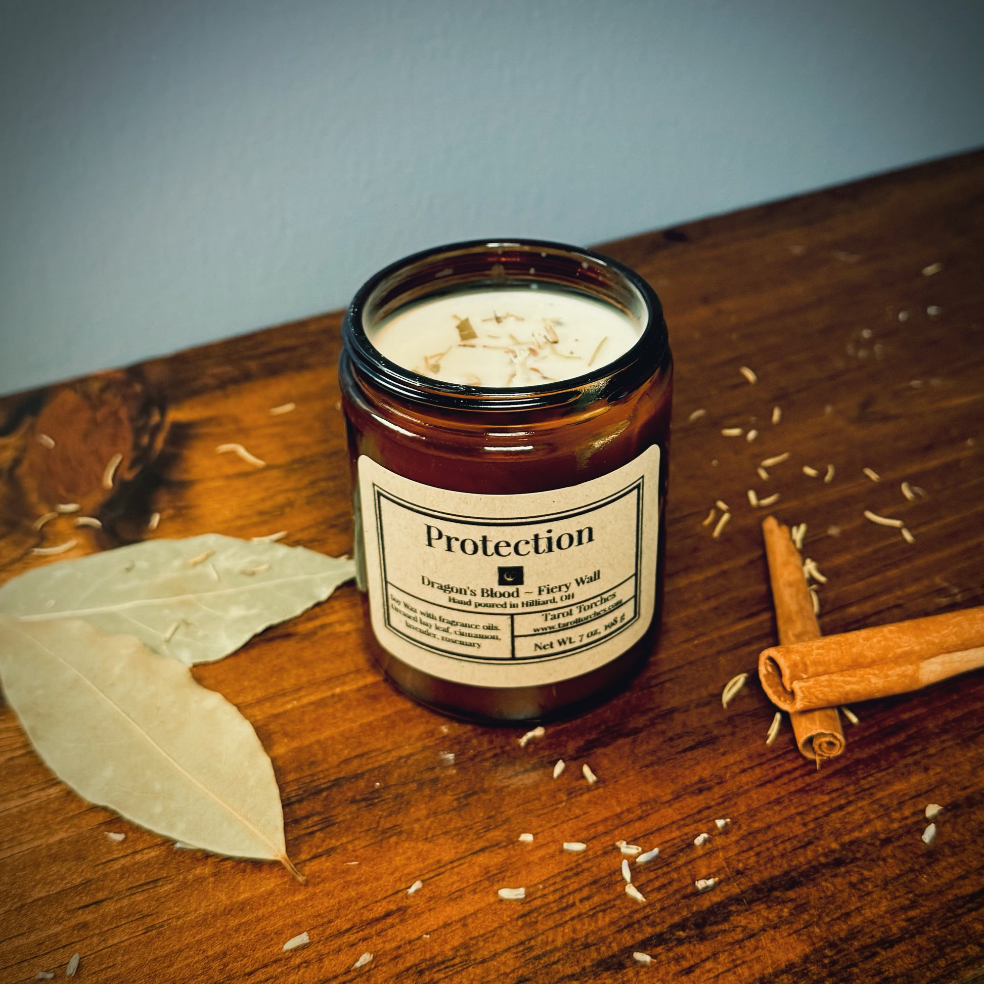 A Protection Ritual Candle with a melted wax layer, surrounded by bay leaves and cinnamon sticks on a wooden surface.
