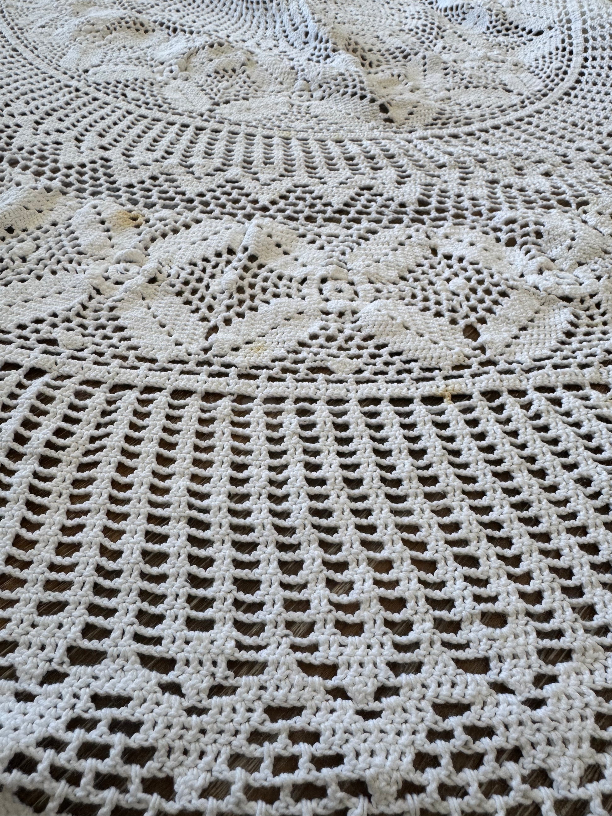 A vintage white crochet tablecloth with an oval shape, displayed on a wooden surface.