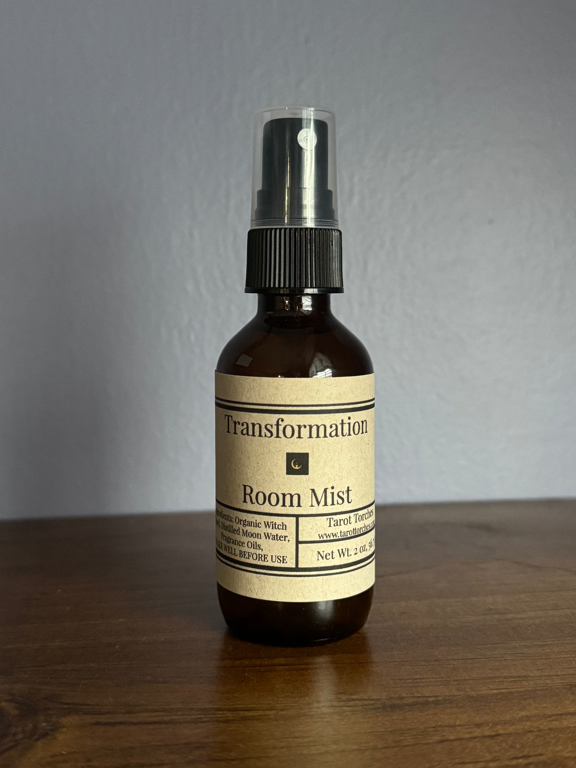 An amber glass spray bottle with a label reading "Transformation" on a wooden surface.