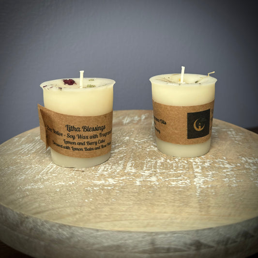 A set of two white votive candles with kraft labels on a white wooden surface.