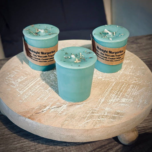 A set of three green votive candles, two with brown kraft labels sitting on a wooden surface.